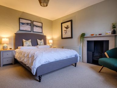 A bedroom with a bed two bedside tables with lamps a fireplace and a green armchair at Sunny Brae in Lindale