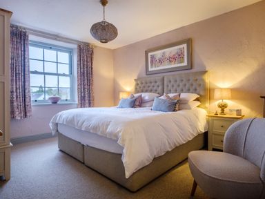 A bedroom with a double bed bedside tables with lamps a window with curtains and an armchair at Sunny Brae in Lindale