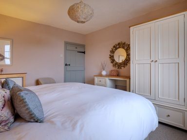 A bedroom with a bed, pillows, a wooden wardrobe, a door, a round mirror above a dresser, and a hanging light at Sunny Brae in Lindale