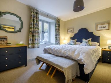 A bedroom with a bed a bench at the foot of the bed curtains and dressers with lamps at Sunny Brae in Lindale