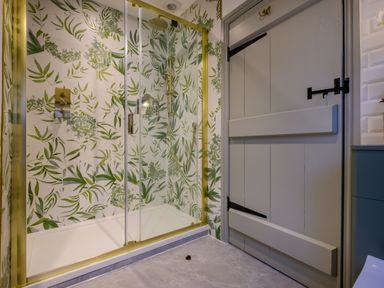 A shower area with glass doors and leafy patterned tiles next to a wooden door in a bathroom at Sunny Brae in Lindale