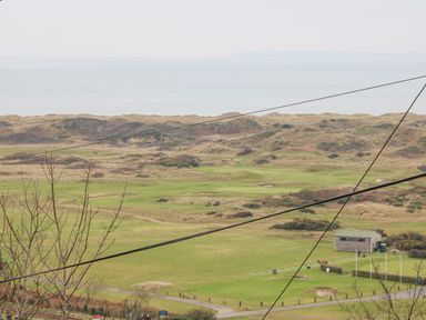A golf course with a building and flagpoles near a coastal area with dunes and the sea in the background at Hafod Y Bryn in Harlech