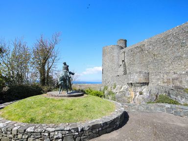 A stone castle with round towers and a statue of a rider on horseback on a grassy mound at Hafod Y Bryn in Harlech