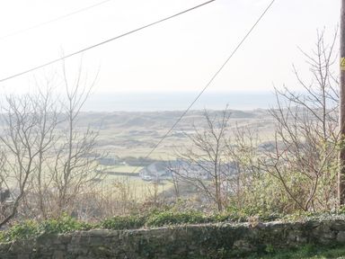 A view of a grassy landscape with leafless trees and houses in the distance at Hafod Y Bryn in Harlech