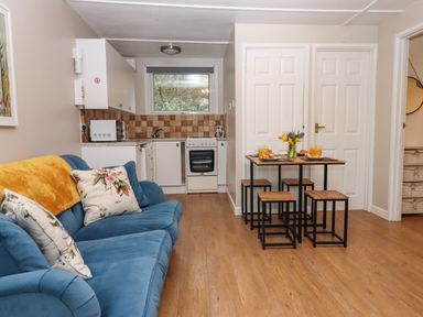 A living room with a blue sofa a dining table with stools and a small kitchen area at 2 The Glade in Kilkhampton