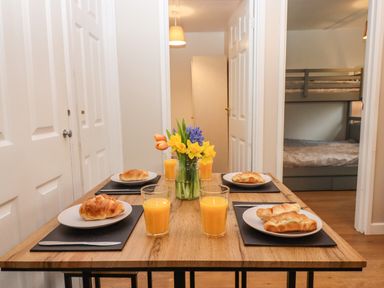 A dining table with plates of croissants and glasses of orange juice with a flower vase in a room at 2 The Glade in Kilkhampton