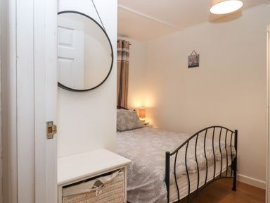A bedroom with a metal bed frame a bedside table with a lamp and a round mirror on the wall at 2 The Glade in Kilkhampton