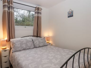 A bedroom with a double bed curtains on a window and bedside tables with lamps at 2 The Glade in Kilkhampton