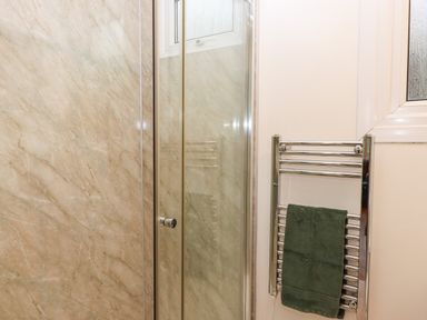 A bathroom with a glass shower door a towel radiator with a green towel and frosted window at 2 The Glade in Kilkhampton