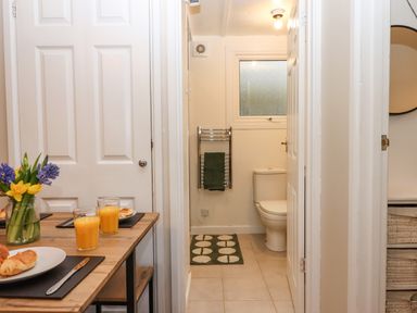 A small bathroom with a toilet and towel rack viewed from a dining area with a table set with croissants and orange juice at 2 The Glade in Kilkhampton