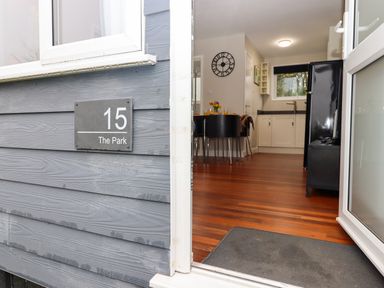 The open entrance door showing a wooden floor dining area with black chairs and a kitchen with white cabinets at 15 The Park in Kilkhampton