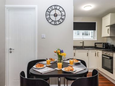 A dining area with a black table set for four with croissants and orange juice in a kitchen at 15 The Park in Kilkhampton