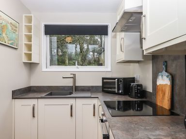 A kitchen with a sink below a window and a countertop with toaster and microwave at 15 The Park in Kilkhampton