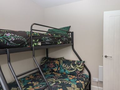 A bunk bed with floral bedding against a white wall near a closed white door at 15 The Park in Kilkhampton