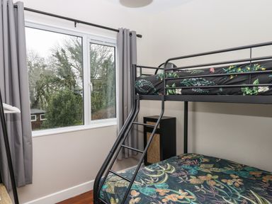 A bedroom with a bunk bed next to a window with curtains at 15 The Park in Kilkhampton