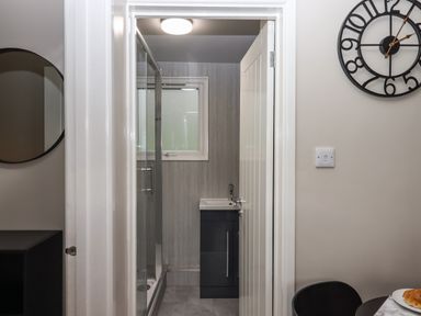 A bathroom with a shower enclosure a sink with cabinet a round wall clock and part of a dining table with food at 15 The Park in Kilkhampton