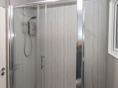 A bathroom shower enclosure with a glass door a mounted shower head and controls at 15 The Park in Kilkhampton