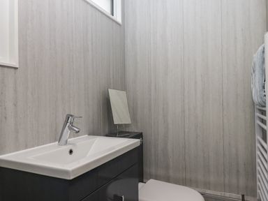 A bathroom with a sink, faucet, small mirror, toilet, and towel on a rail at 15 The Park in Kilkhampton
