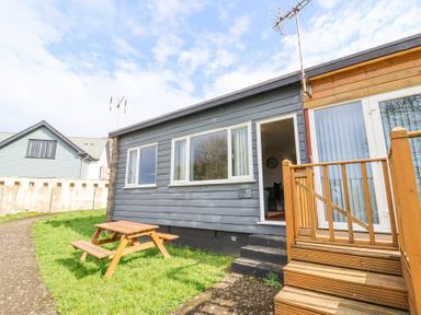 A small gray house with a wooden staircase and picnic table outside at 15 The Park in Kilkhampton