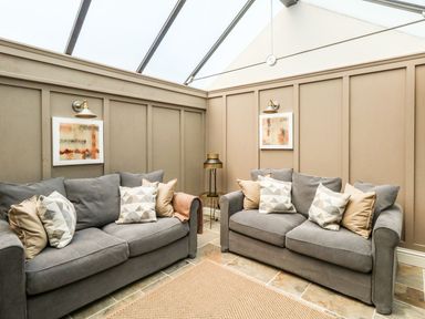 A seating area with two gray sofas with pillows and a small round table with a lamp between them at The Apple Loft at Jordan House in Preston