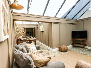 A living area with a gray sofa and cushions a dining table set with chairs a television on a wooden stand and a woven pouf at The Apple Loft at Jordan House in Preston