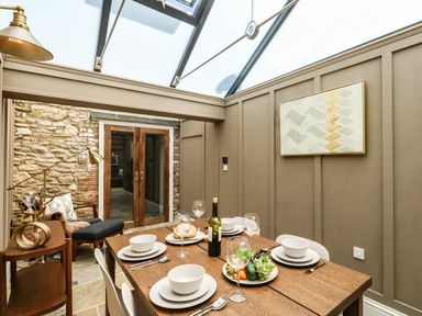 A dining area with a wooden table set for six under a glass ceiling at The Apple Loft at Jordan House in Preston