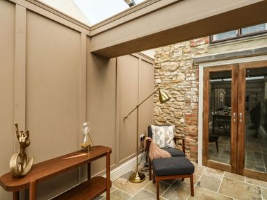 A small seating area with a chair and ottoman next to a floor lamp and a wooden table with decorative items by stone wall and glass double doors at The Apple Loft at Jordan House in Preston