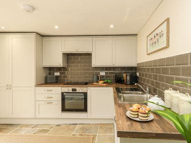 A kitchen with white cabinets a built in oven a microwave a sink and muffins on the counter at The Apple Loft at Jordan House in Preston