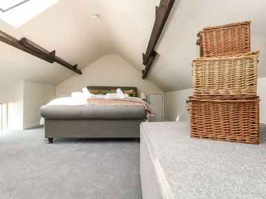 A bedroom with a bed and stacked wicker baskets under a sloped ceiling with exposed beams at The Apple Loft at Jordan House in Preston