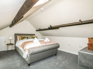 A bedroom with a grey bed under a sloped ceiling with exposed wooden beams at The Apple Loft at Jordan House in Preston