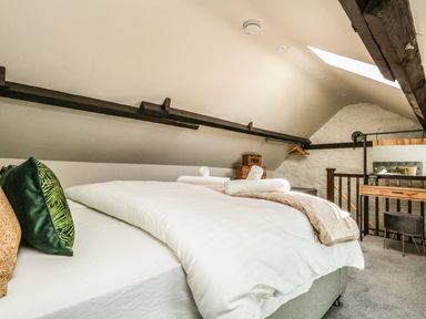 A bedroom with a bed with white bedding pillows and towels wooden beams skylight and a dressing table at The Apple Loft at Jordan House Preston