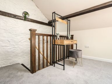 A small wooden vanity with a mirror and two plants beside a wooden staircase railing in a carpeted room at The Apple Loft at Jordan House in Preston