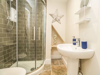 A bathroom with a glass shower cubicle a white sink with blue accessories and a wall decoration at The Apple Loft at Jordan House in Preston