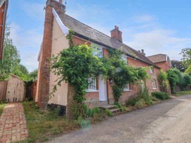 A brick cottage with plants growing on the walls and a wooden gate beside it at Brook Cottage in Peasenhall