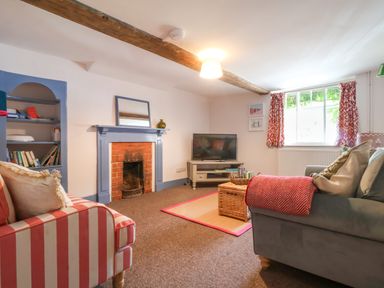 A living room with a fireplace a television striped and gray sofas and a window with red curtains at Brook Cottage in Peasenhall