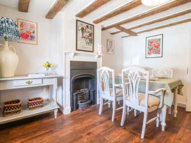 A dining room with a table and chairs a side table with a lamp and baskets and a fireplace at Brook Cottage in Peasenhall