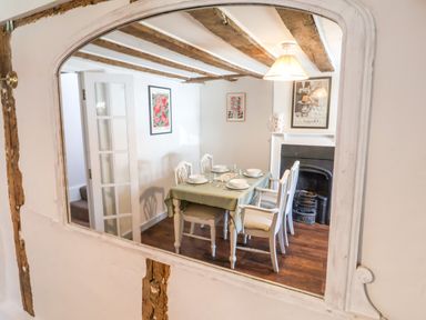 A dining room with a table set for four near a fireplace and wooden ceiling beams at Brook Cottage in Peasenhall