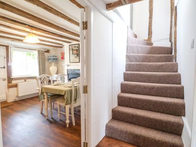 A carpeted staircase next to a dining area with a table set for four and exposed wooden beams at Brook Cottage in Peasenhall