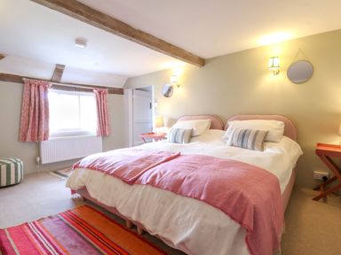 A bedroom with a double bed and pink blankets and a window with patterned curtains at Brook Cottage in Peasenhall