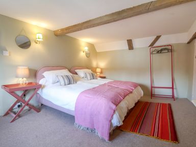 A bedroom with a double bed two bedside tables with lamps wall mirrors a clothing rack and a striped rug at Brook Cottage in Peasenhall
