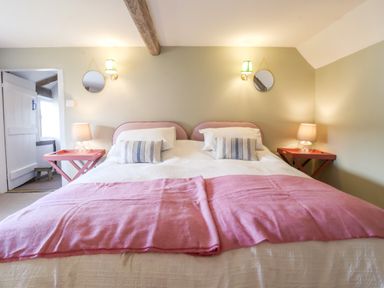 A bedroom with a double bed pink blankets bedside tables with lamps and round mirrors at Brook Cottage in Peasenhall