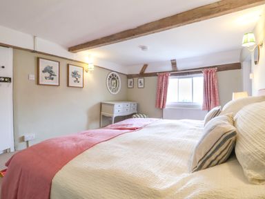 A bedroom with a large bed a bedside lamp a window with curtains framed pictures a mirror and a desk at Brook Cottage in Peasenhall