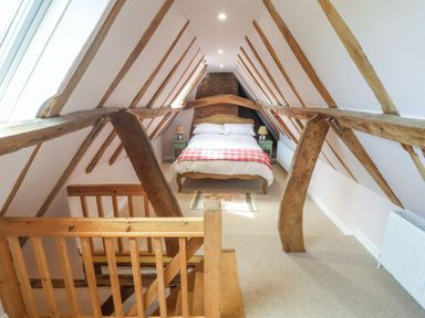 A bedroom with a double bed wooden beams and a staircase at Brook Cottage in Peasenhall