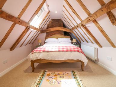 A bedroom with a bed a red and white blanket exposed wooden beams and a skylight at Brook Cottage in Peasenhall