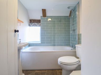 A bathroom with a bathtub shower combination toilet and sink with blue tiled wall at Brook Cottage in Peasenhall