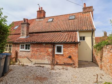The back of a brick house with a tiled roof and two chimneys with a gravel yard and trash bins at Brook Cottage Peasenhall