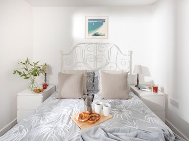 A bedroom with a double bed with gray patterned bedding two bedside tables with lamps a plant and snacks on a tray on the bed at Wheal Amelia Lodge Wendron near Helston