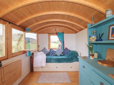 A wooden room with a daybed with blue cushions and blankets and a blue cabinet with items on it at Harris Hut in Bishops Lydeard