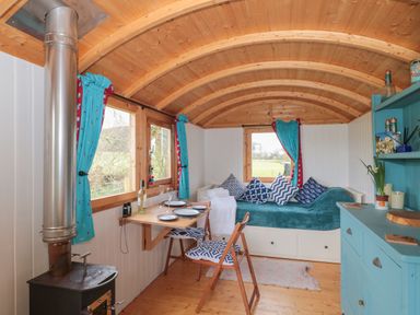 A wooden room with a stove and a small dining table next to a window at Harri's Hut in Bishop's Lydeard