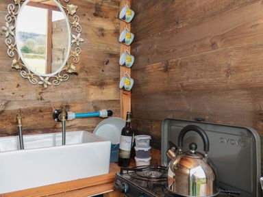 A kitchen corner with a sink a gas stove a kettle cups hanging on a wooden wall and a decorative mirror at Harris Hut in Bishops Lydeard